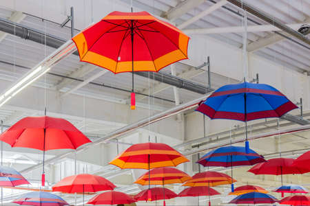 Multicolored collapsible umbrellas - red, blue, orange, suspended near the ceiling of the office buildingの写真素材