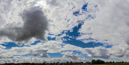 Sky with cumulus clouds in the countryside on the of field, buildings and trees in summer day