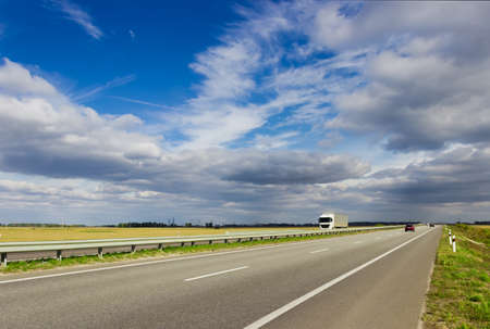 Highway among fields on a background of sky with cumulus and cirrus clouds