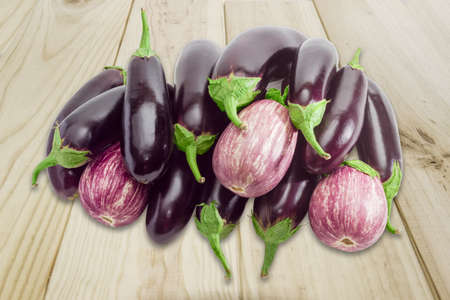 Pile of a ripe purple conventional eggplant and graffiti eggplant on a wooden surfaceの写真素材
