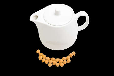 Shelled apricot kernels and white ceramic teapot on a black background. Isolation.の写真素材