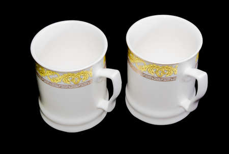 Two white porcellaneous cups with yellow and aureate floral ornaments on a black background. Isolation.の写真素材