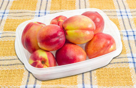 Ripe nectarines in a transparent plastic tray on a checkered tablecloth closeupの写真素材