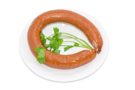 Ring sausage in natural casing with branches of coriander on a white plate on a light backgroundの写真素材