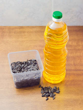 Striped sunflower seeds in transparent plastic tray, a few seeds separately and bottle of sunflower oil on a wooden surfaceの写真素材