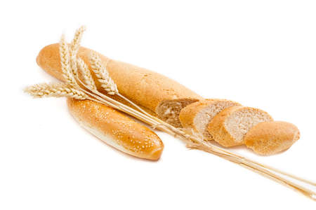 Long thin loaf of wheat bread with bran, partially sliced, bun, sprinkled with sesame seeds and bunch of wheat spikes closeup on a light background. Isolationの写真素材