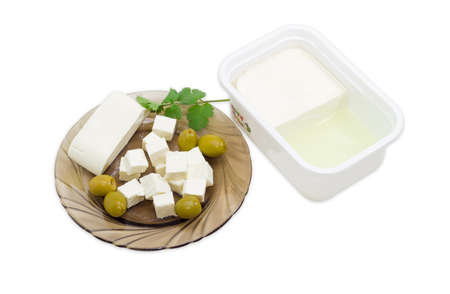 Rectangular container of feta cheese in a brine and sliced cheese, olives and a small branch coriander on a saucer on a light backgroundの写真素材