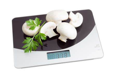 Several uncooked wholes and halfs of champignon mushroom and one leaf of fresh parsley on digital kitchen scale on a light background. Isolationの写真素材