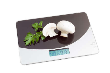 Home digital kitchen scale with a two champignon mushrooms and branch of parsley on working surface on light background. Isolationの写真素材