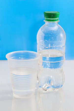 Small water bottle and transparent disposable plastic cup with water on a blue backgroundの写真素材