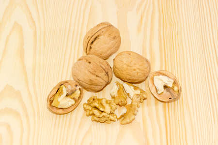 Three ripe whole walnuts in shell, one walnut splited in half and several nut kernels closeup on a wooden surfaceの写真素材