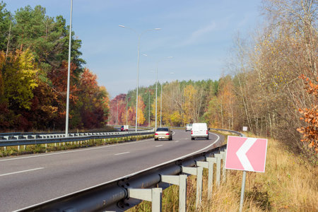 Fragment of the motorway with asphalt road surface and road surface marking, lampposts, traffic barriers and forest on both sides autumn morningの写真素材
