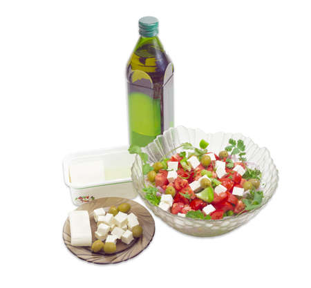 Greek salad in a glass salad bowl, bottle olive oil, container of feta cheese in a brine and sliced cheese and olives on a saucer on a light backgroundの写真素材