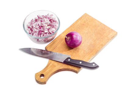 Chopped red onion in a glass bowl, peeled whole onion and kitchen knife on a wooden kitchen cutting board on a light background. Isolation.の写真素材