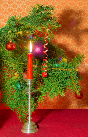 Branches of a decorated Christmas trees and candle in a candlestick on a red backgroundの写真素材