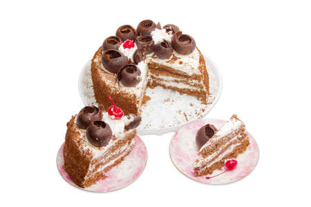 Cut round sponge cake, decorated with chocolate, whipped cream and frozen cherries and two pieces of cake on a pink saucers on a light background. Isolationの写真素材