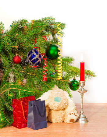 Fragment of a decorated Christmas trees, candle in a candlestick, soft  toy and Christmas Gift on a light backgroundの写真素材