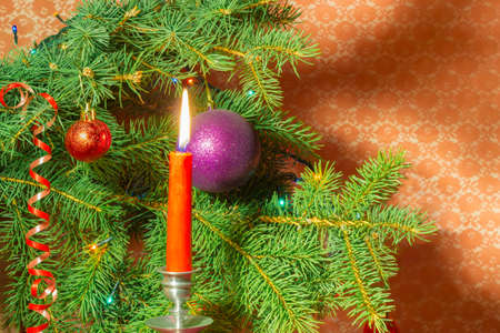 Branch of a Christmas trees, decorated with Christmas ornament and lights and candle in a candlestick closeup on a red backgroundの写真素材