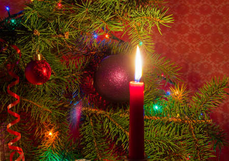 Burning red candle on a background of decorated Christmas tree closeupの写真素材