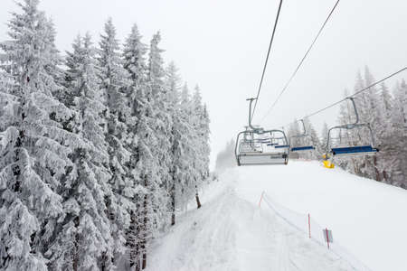 Chairlift and ski piste among the spruce forest at ski resort in cloudy weatherの写真素材