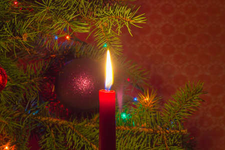 Burning red candle on a background of decorated Christmas tree closeupの写真素材