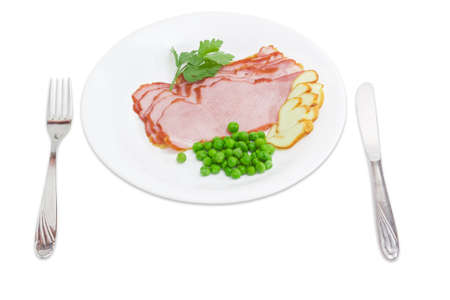 Several slices of the ham and smoked cheese with a boiled green peas and a sprig of parsley, fork and knife on a white dish on a light background.の写真素材