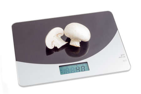 Household digital kitchen scale with one whole and one half of a mushroom on working surface on light backgroundの写真素材