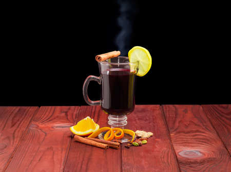 Mulled wine in glass mug with slice of lemon and mulling spices for cooking a mulled wine on dark red wooden surface against a dark backgroundの写真素材