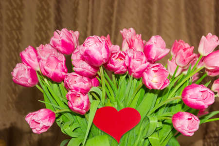 Large bouquet of pink tulips and heart made of red paper on a brown backgroundの写真素材