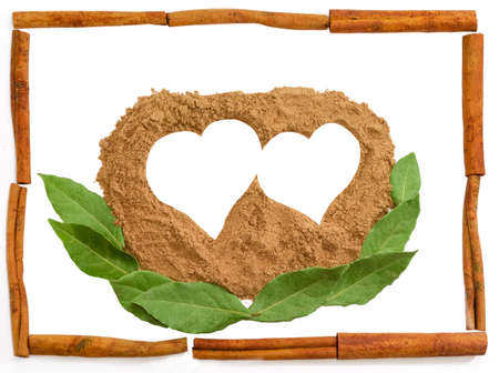 Pile of powder cinnamon in the shape of a two hearts and a bay leaves with a frame made up of...