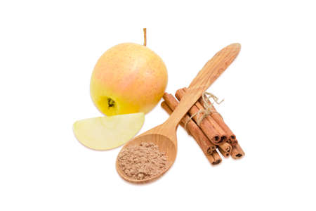 Several cinnamon sticks tied by twine, cinnamon powder in a wooden spoon and one whole apple and piece of apple on a light backgroundの写真素材