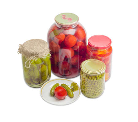 Two pickled cucumbers and one pickled tomato on a saucer and pickled cucumbers, tomatoes, bell pepper and green peas in glass jars on a light backgroundの写真素材
