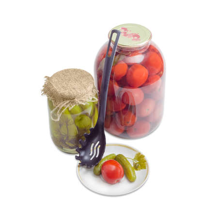 Two pickled cucumbers and one pickled tomato on a saucer, two various glass jars with pickled cucumbers and tomatoes and black plastic slotted spoon on a light backgroundの写真素材