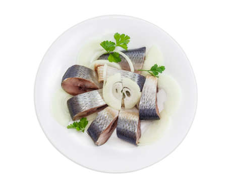 Sliced pickled atlantic herring, chopped onions and parsley leaves on a white dish on a light backgroundの写真素材
