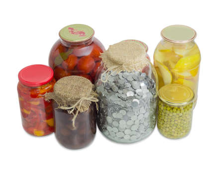 Coins of the Ukrainian hryvnia in big glass jar for home canning among canned fruit and canned vegetable on a light backgroundの写真素材