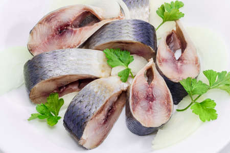 Sliced pickled atlantic herring, chopped onions and parsley leaves on a white dish closeupの写真素材