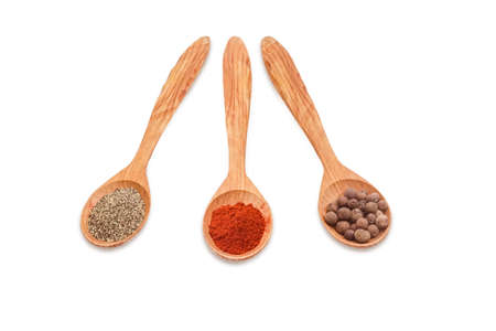 Three wooden spoons of various kinds of pepper - ground black pepper, chili powder and allspice on a light backgroundの写真素材