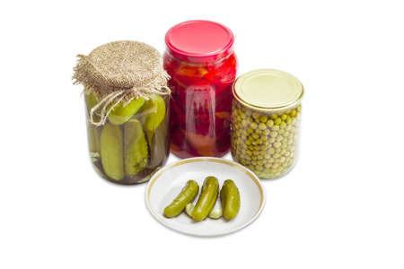 Several pickled cucumbers on a saucer and pickled cucumbers, pickled bell pepper and pickled green peas in glass jars on a light backgroundの写真素材