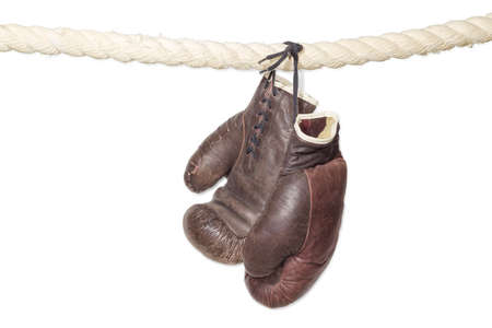 Old worn leather brown boxing gloves, that hang on a laces on the rope of a boxing ring on a light background.の写真素材