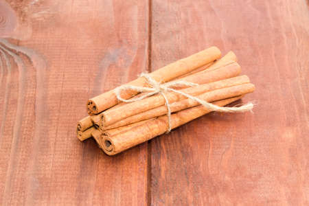 Several cinnamon sticks tied by twine on a surface with wooden planks closeupの写真素材
