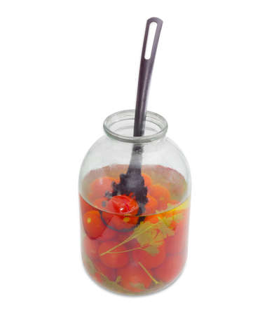 Pickled tomatoes and black plastic slotted spoon in opened glass jar on a light backgroundの写真素材