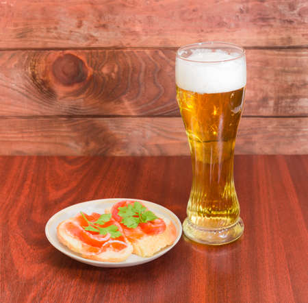 Beer glass with lager beer and two sandwiches made with a salted trout on saucer on wooden table against the backdrop of dark wooden planksの写真素材