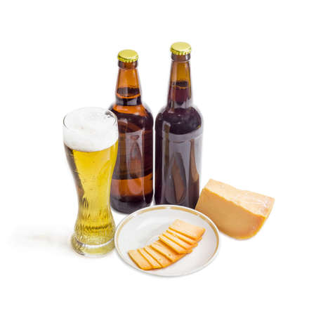 Beer glass with lager beer, two bottles beer, one piece and several thin slices of hard cheese on saucer on a light backgroundの写真素材
