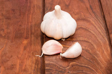 Garlic bulb and two garlic cloves on the surface of the dark wooden planks closeupの写真素材