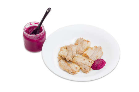 Several slices of roast pork with horseradish sauce on white dish and small glass jar of horseradish with red beet on a light backgroundの写真素材