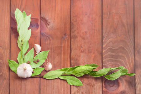 Frame of the two  dried branches of a bay laurel, laid out on the left and at the bottom with an empty space in the center, garlic and few peas allspice on a surface with wooden planksの写真素材