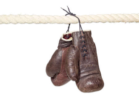 Old worn leather brown boxing gloves, that hang on a laces on the rope of a boxing ring on a light background.の写真素材