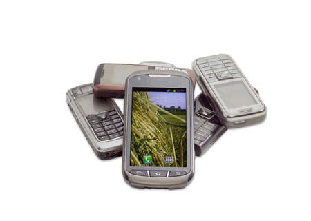 Modern smartphone with touchscreen on the background of several old shabby outdated mobile phones on a light backgroundの写真素材
