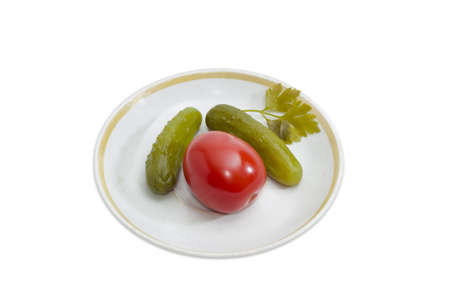 Two pickled cucumbers and one pickled tomato on a saucer on a light backgroundの写真素材