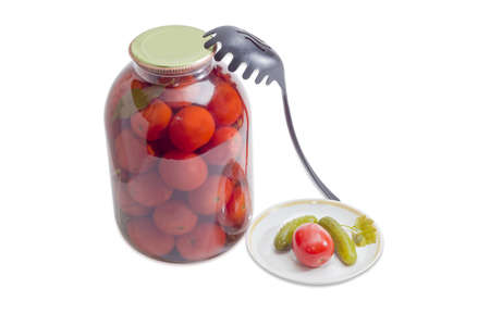 Glass jar with canned tomatoes, two canned cucumbers and one canned tomato on a saucer and black plastic slotted spoon on a light backgroundの写真素材